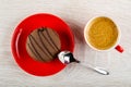 Twin cookie with cream filling in saucer, spoon, cup of coffee on wooden table. Top view