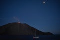 A Stromboli volcano spews lava while a sailboat sails past, with the moon above