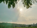 Strong afternoon sunlight in summer shining through cloudy sky onto hills, green leaves, and the ground below