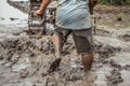 Strong asian farmer driving tiller tractor in muddy field, detail of male farmer walking barefoot in deep mud Royalty Free Stock Photo