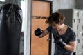 strong Asian youn man punching sandbag with gloves in sport gym