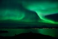 Strong aurora borealis over fjord and mountain with tourist in front