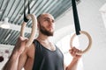 Muscular man holding gymnastic rings at light gym and looking away Royalty Free Stock Photo