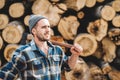Strong bearded lumberjack wearing plaid shirt hold ax in hand on background of sawmill