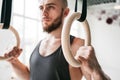 Strong bearded man holding gymnastic rings at gym