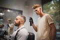 Young barber with a hair spray working on a blurred background. Stylish client in barber shop Barber occupation concept.