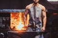 Strong blacksmith is posing for photographer at his workshop