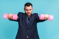 Strong bossy businessman wearing official style suit stretching arms with pink dumbbells, looking at