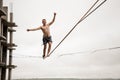 Strong brave man balancing on a slackline high against empty building and sky