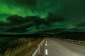 Strong bright Aurora Borealis behind heavy clouds over road, Joesjo Lake and Scandinavian mountains in Swedish Lapland look very