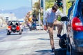 A strong businessman is bending his knee while trying to change a flattie on his car with his lug wrench