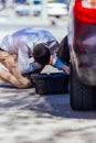 A strong businessman is bending his knee while trying to change a flattie on his car with his lug wrench