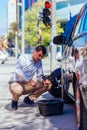 A strong businessman is bending his knee while trying to change a flattie on his car with his lug wrench