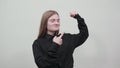 Strong caucasian young woman showing muscules, pointing finger on it.