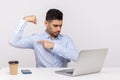 Strong confident man boss sitting office workplace, showing biceps to laptop screen when talking on video call, feeling power