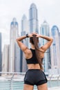 Strong fit female athlete getting ready for workout towards the skyscrapers. Strong fitness woman tying ponytail. Motivation and Royalty Free Stock Photo