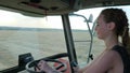 Strong girl driving behind wheel of tractor in field during harvesting