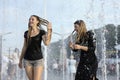 Strong heat in the city: laughing girls playing with fountain water jets at the square Royalty Free Stock Photo