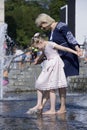 Strong heat in the city: woman and little girl playing with fountain water jets at the square Royalty Free Stock Photo