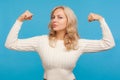 Strong independent woman with blond hair looking at camera showing her arm muscles, proud of her strength and leadership skills, Royalty Free Stock Photo