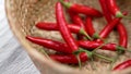 Strong intensity red chili peppers falling into a rustic braided bowl.