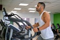 Strong Latin man doing elliptical training at a gym.