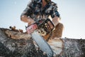 Strong lumberjack wearing plaid shirt and hat use chainsaw in sawmill Royalty Free Stock Photo