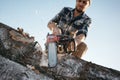 Strong lumberjack wearing plaid shirt and hat use chainsaw in sawmill Royalty Free Stock Photo