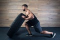 A man in a tank top and shorts with a beard tries to push a tire in a gym