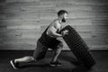 A bodybuilder with a tattoo and beard is pushing a tire in a gym