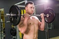 Strong man - bodybuilder with dumbbells in a gym, exercising with a barbell.