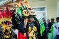 Strong man in bright costume carries scary mask by city street at dominican carnival