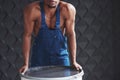 Strong man leaning on barrel. Young african american worker in blue uniform have a break on his job Royalty Free Stock Photo