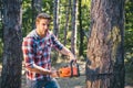 Strong man lumberjack with an axe or chainsaw in a plaid shirt. A handsome young man with a beard carries a tree.