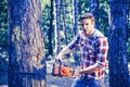 Strong man lumberjack with an axe or chainsaw in a plaid shirt. A handsome young man with a beard carries a tree. Royalty Free Stock Photo