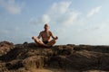 The white man is meditating on the top of the old cliff.