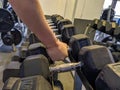 Strong man`s hand picking up a dumbbell from organized line of heavy dumbbell equipment in a modern gym for lifting weight and Royalty Free Stock Photo