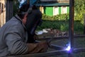 A strong man is a welder, welding mask and welders leathers, a metal product is welded with a arc welding machine at the