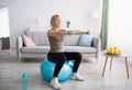 Strong mature woman working out with dumbbells on fitness ball at home, blank space