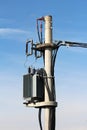 Strong metal electric power transformer with grey utility box mounted on high concrete utility pole and connected with electrical Royalty Free Stock Photo