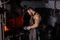 Strong muscular blacksmith prepares iron on fire