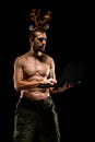 Strong muscular man with deer antlers holding laptop isolated on black background Royalty Free Stock Photo