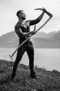 Strong muscular power sexy farmer using scythe. Farmer with a scythe on green grass field. Guy cut grass. Rural farmer