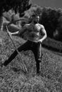 Strong muscular power sexy farmer using scythe. Farmer with a scythe on green grass field. Guy cut grass. Rural farmer