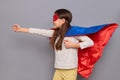 Strong powerful little girl wearing superhero costume and mask isolated over gray background pretending flying with raised fist Royalty Free Stock Photo