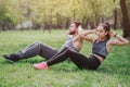 Strong and powerful people are working out outside in park. They are doing abs exercises. Young man and woman look