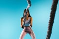A strong, pumped-up girl in sport leggings throws a battle rope towards the camera. Blue background and empty side ad