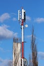 Strong red and white metal pole with various shapes and sizes cell phone transmitters and antennas next to tall building and