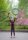 Strong slender young cyclist in a helmet lifts her bike cheerfully and vigorously over her head. cycling outdoors Royalty Free Stock Photo