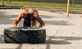 Strong sporty guy flipping workout wheel at outside gym Royalty Free Stock Photo